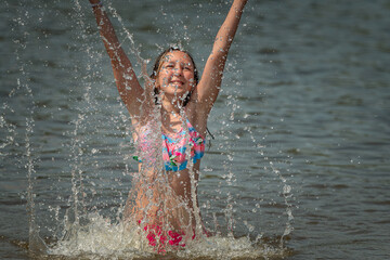 A little girl splashes in a pond during the day.