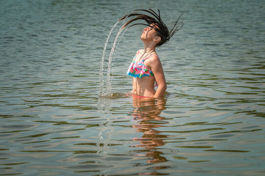 A little girl splashes in a pond during the day.