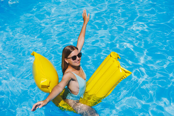 Summer lifestyle portrait of beautiful woman in sunglasses floating on inflatable mattress in...