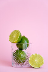 green and fresh limes in faceted glass on pink background.