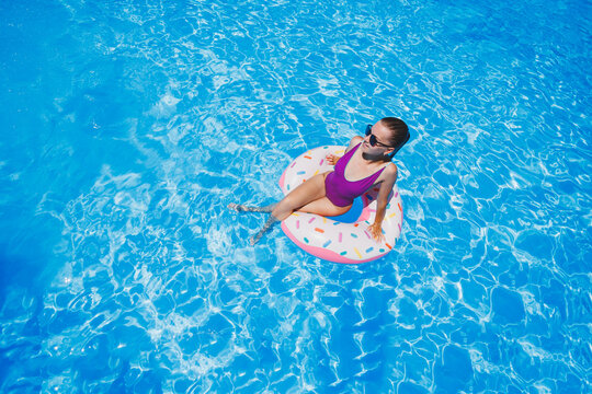 Slim woman in sunglasses in the pool in an inflatable swimming ring in a bright swimsuit, summer photo, swimming photography, summer woman photos. Beach fashion