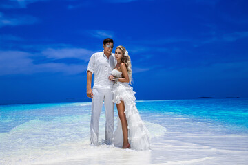 Summer love. Beautiful happy young couple in wedding clothes is standing on a beach in the Maldives. Engagements and wedding on the beach on the paradise island of Maldives. Luxury travel.