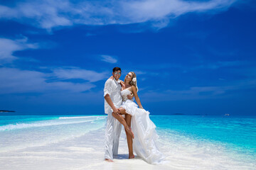 Summer love. Beautiful happy young couple in wedding clothes is standing on a beach in the Maldives. Engagements and wedding on the beach on the paradise island of Maldives. Luxury travel.