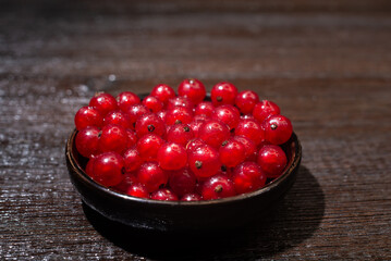 Red currants in a black bowl on a wooden background. Harvest of ripe summer berries