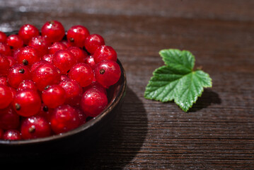 Red currants with leaves in a black bowl on a wooden background. Harvest of ripe summer berries. Closeup