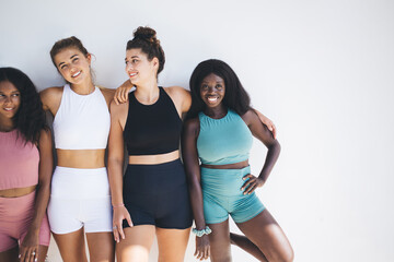 Joyful group of women with different figure sizes smiling together in sportswear on white...