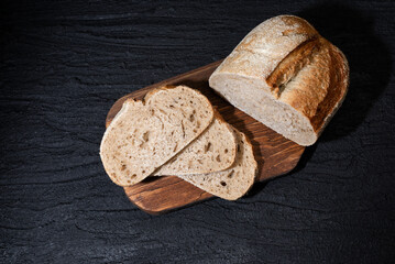 Sliced yeast grain bread with oats on dark concrete background