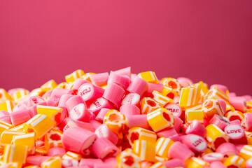 Bunch of pink with inscription Love and yellow striped caramel candies on pink background. Mix of colorful sweetmeat lollipops close up. Sweet sugar dessert. Candy Shop.