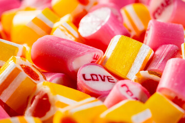 Bunch of pink with inscription Love and yellow striped caramel candies. Mix of colorful sweetmeat lollipops. Sweet sugar dessert for a holiday or children's birthday. Candy Shop. Extreme close up.