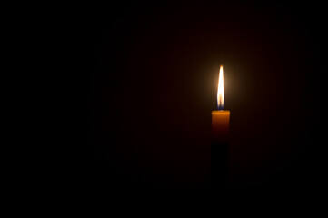 Single small yellow candle light glowing isolated on black or dark background on table in church or...