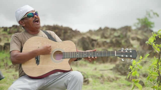 Enjoying middle aged hiker singing song by playing guitar on top of hill - concept of hobby, entertainment, wellness and selfcare.