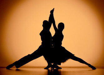 Couple of dancers are dancing elements of Argentine tango. Black silhouettes of man and woman on an orange brown gradient background in studio. Screensaver for school of ballroom Latin American dances
