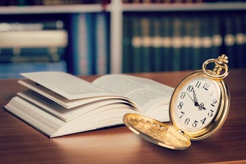 Antique pocket watch on opened old book on background.