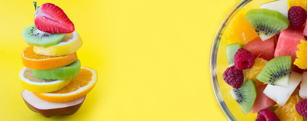 Banner. Pyramid of chopped fruit and vegetable in balance and fruit salad in the glass bowl on the yellow background. Closeup. Copy space.