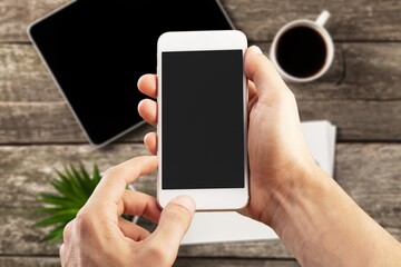 Man holding a smartphone with black screen on office table.