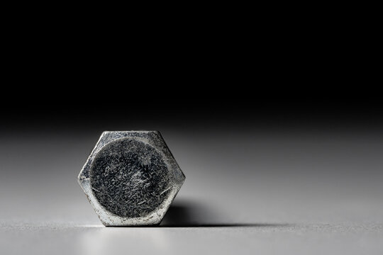 The head of a hexagonal metal bolt on a gray black background. Stainless steel bolt for screwing, fastening, fixing. Metal construction anchor for hardware store and furnitures.