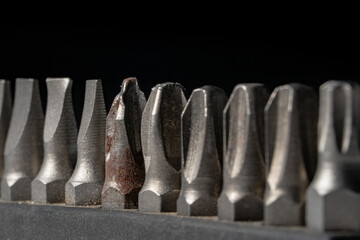Set of bits for screwdriver on black background. Metal nozzles straight and cruciform shape for...