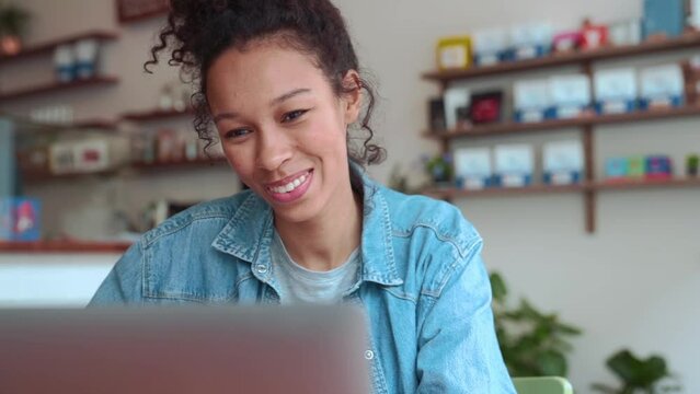 Positive woman with afro hair talking by video call on laptop in cafe