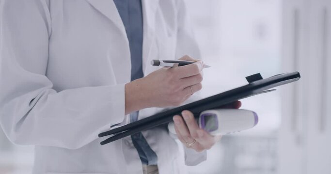 Closeup Of A Doctor Writing Covid Patients Chart During A Checkup Holding A Thermometer. Taking Temperature Reading Measurements And Adhering To Corona Virus Pandemic Protocol