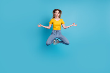 Portrait of sportive active girl in motion jumping over in the air isolated on blue background doing zen