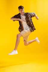 Fototapeta na wymiar Full-length man's portrait isolated on bright yellow studio backgroud. Young emotional man jumping. Human emotions, facial expression concept.