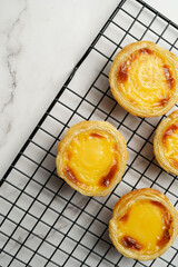 Traditional portuguese vanilla pudding puff pastry pastel de nata on black oven rack on marble background - top view