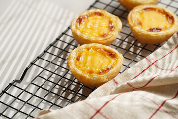 Traditional portuguese vanilla pudding puff pastry pastel de nata on black oven rack on marble background with checkered kitchen towel