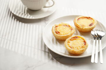 Traditional portuguese vanilla pudding puff pastry pastel de nata on black oven rack on white plate with a cup of coffee in white porcelain