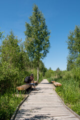 The hiker sits on a wooden bench by the wooden boardwalk in a wetland.