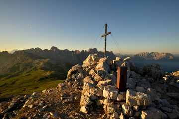 Das Gipfelkreuz auf dem Monte Petz in den S&uuml;dtiroler Dolomiten im der Morgensonne und im Hintergrund sieht man die Rosengarten- und Latemar Gruppe.