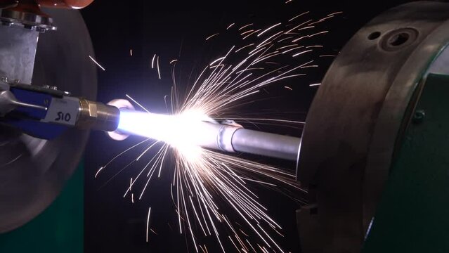 Thermal spray metal coating process. Steel rotating detail during powder flame spraying process at a metallurgical plant. Automatic industry robotic welding machine. Plasma welding with flying sparks.