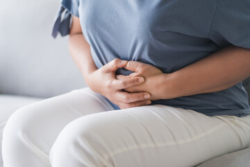 Woman suffering from stomachache sitting on the sofa at home. abdominal pain, Gastritis, Period, menstruation.