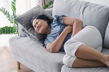 Woman suffering from stomachache lying down on the sofa at home. abdominal pain, Gastritis, Period, menstruation.