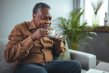 Close up shot of an elderly man sitting at home drinking coffee. Senior businessman having a coffee...