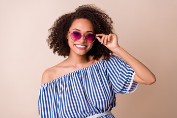 Photo of positive pretty lady wear striped outfit arm dark glasses smiling isolated beige color background
