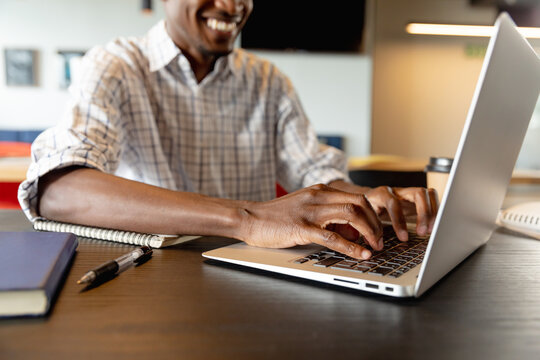 Midsection of smiling african american young businessman using laptop in creative office