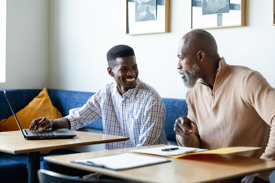 Smiling african american businessmen discussing over laptop at desk in creative office