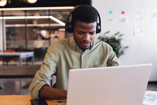 African american young businessman wearing headphones using laptop in office