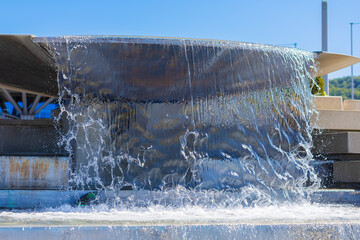 A stream of clear water pouring from a large bowl. Cascading street fountain decorating the city