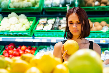 young woman in supermarket choosing grapefruits