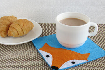 Breakfast with croissant and cocoa. The cup stands on a felt cup coaster.