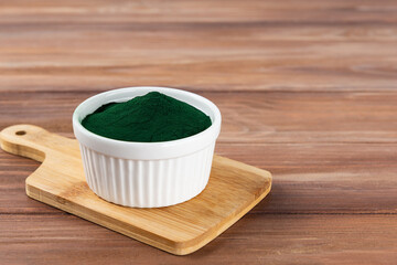 Spirulina powder in a bowl on a wooden board.