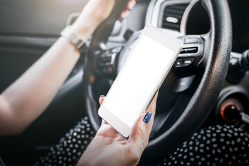 female hand holds a mobile phone with a blank white screen in the car interior. mockup. copy space