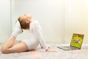 Little gymnast in a white leotard at home, studying remotely. Gymnastics lessons at home....