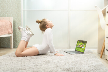 Little gymnast in a white leotard at home, studying remotely. Gymnastics lessons at home....