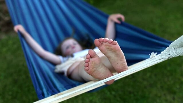 closeup of little girl's feet relaxing in the blue hammock during her summer vacation in the back yard