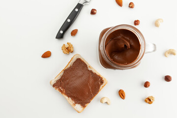 Bread with chocolate paste. A jar of chocolate paste, a knife and various types of nuts. Cashew, almond, walnut, hazelnut, isolated on white background.