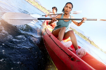 Two serious friends kayaking on a lake together during summer break. Focused and stern women...