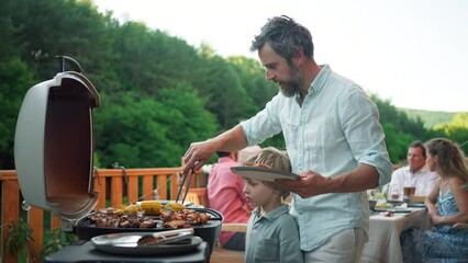 Man grilling ribs and vegetable on grill during family summer garden party, close-up