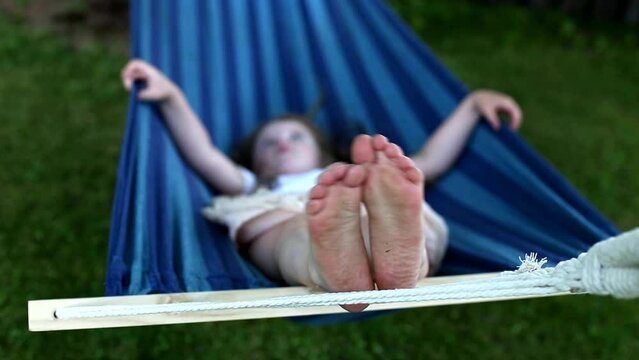 closeup of little girl's feet relaxing in the blue hammock during her summer vacation in the back yard